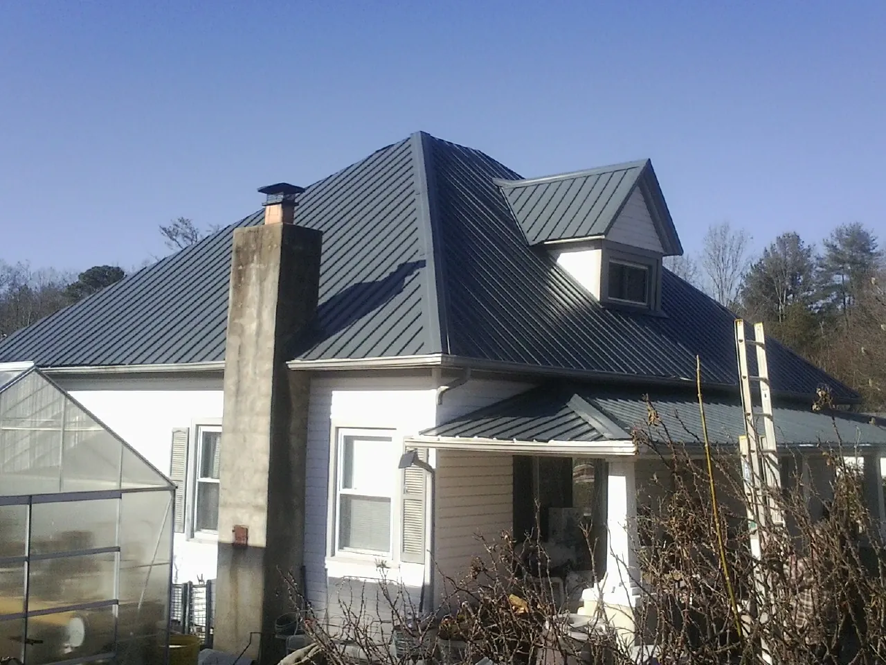 Dark blue standing seam metal roof on a white farmhouse with dormer — Slate & Tile Roof Repair by Roofing Brothers in Delta